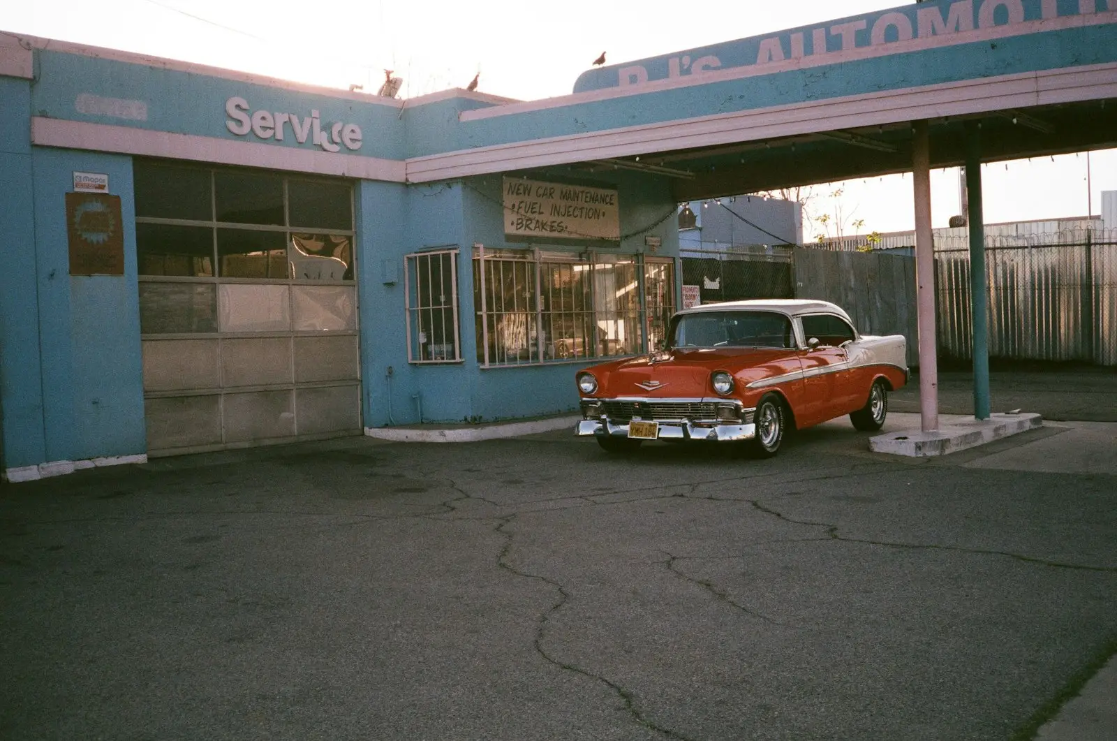 Red and white vintage car parked beside blue and white building during daytime