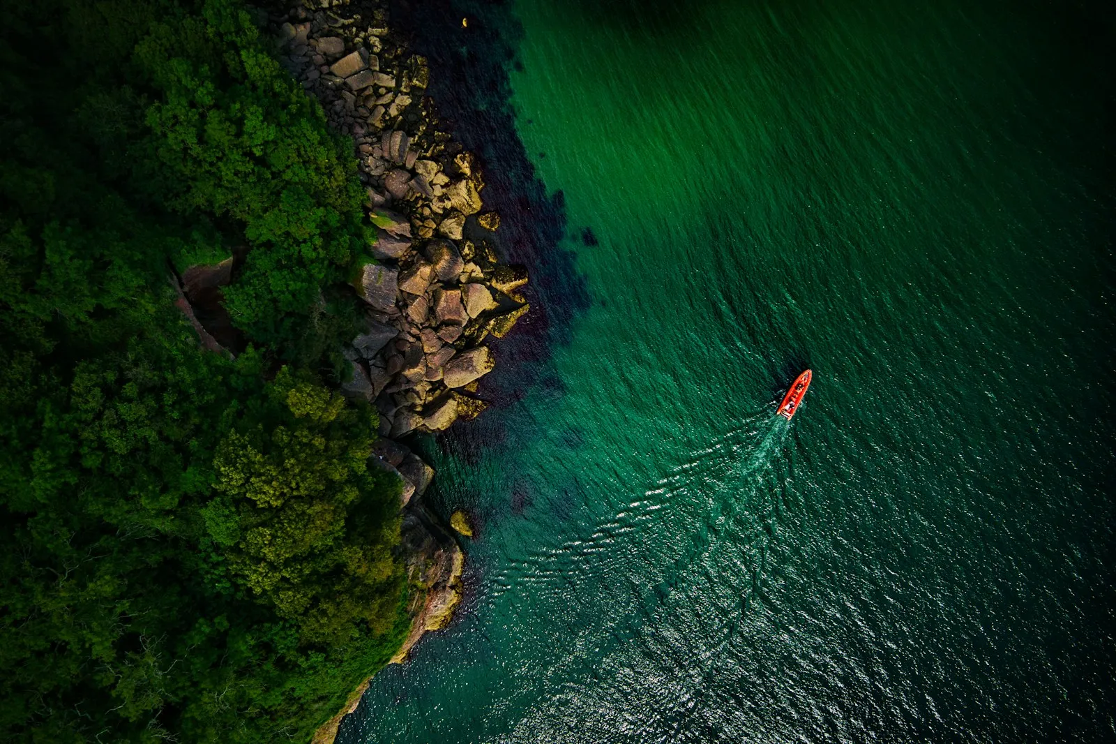 Red Rocks - A red powerboat hugs the shore on a beautiful Summer morning in Devon, UK